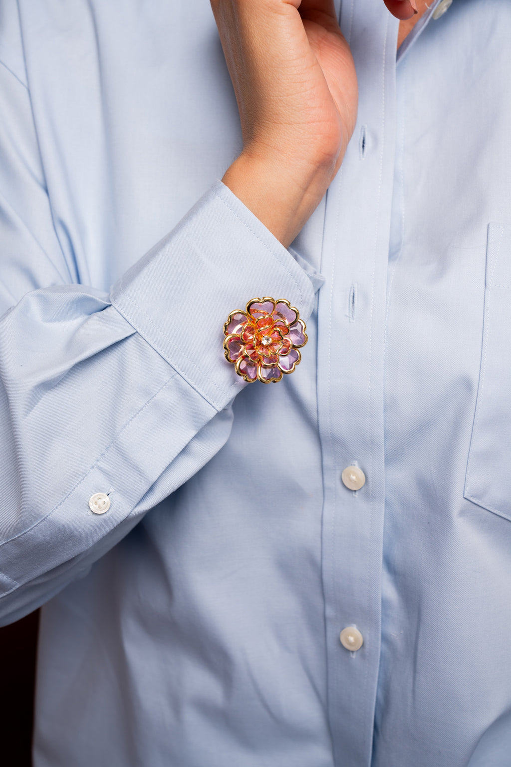 Close-up of a light blue blouse featuring an pink floral button cover detail on the cuff.